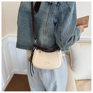 Détail d'un sac en cuir crème avec le texte Aitumi 1986 et une bandoulière tissée chic