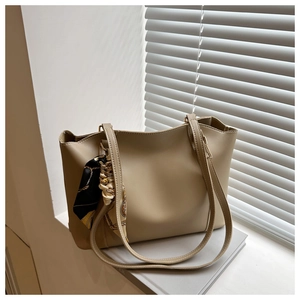 Detail shot of a beige tote bag with a geometric print silk scarf on the leather handle