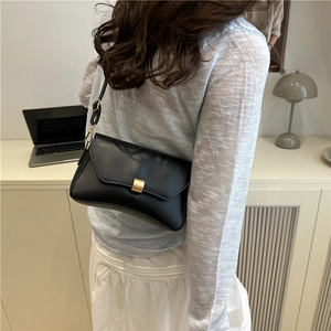 Minimalistische schwarze Unterarmtasche mit goldener Schnalle für Damen auf dem Tisch