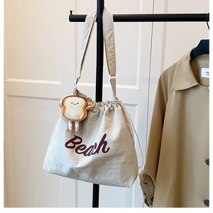 Detail of off-white canvas tote bag with purple Beach text and cute toast plush pendant