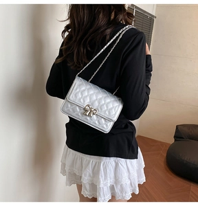 Sac argenté matelassé avec fermoir nœud métallique porté par un mannequin dans un intérieur