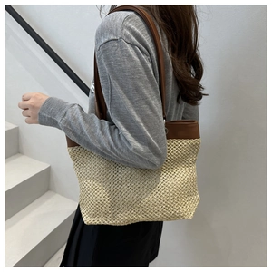 Detail of woven straw tote bag with brown faux leather strap and grid pattern