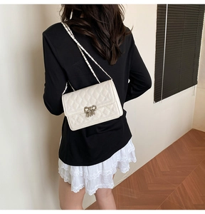 Détail du sac bandoulière matelassé blanc avec nœud argenté et bandoulière chaîne