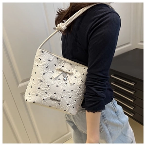 Detail of white embossed underarm bag with black bows and heart-shaped silver pendant