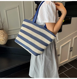 Detailed view of large blue and white striped woven tote bag worn on a woman's shoulder