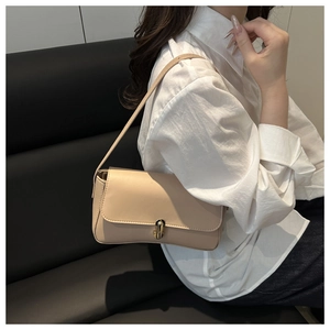 Detail view of a beige minimalist baguette bag with gold metal lock on dark leather seat