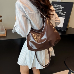 Sac cabas en similicuir marron foncé brillant avec chaîne argentée porté sur le dos