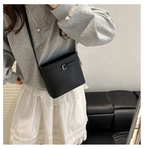 Detail showing the matte black bucket bag with metallic buckle and embossed logo