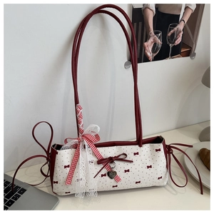 Détail du sac sous le bras en toile crème avec motifs nœuds rouges et pendentif cœur
