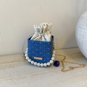 Close-up of blue denim bucket bag with white polka dot embroidery and pearl handle strap