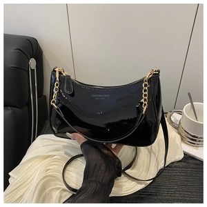 Détail du sac sous le bras en cuir verni noir avec chaîne dorée et logo gravé