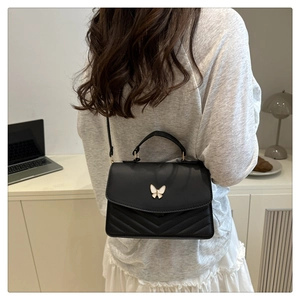 Détail du sac à bandoulière noir matelassé chevron avec fermoir papillon doré sur modèle