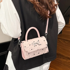 Sac à main en cuir plissé rose avec imprimés nœuds porté par un mannequin en intérieur