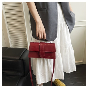 Detail of red patent leather crossbody bag held by a model in a stylish interior setting