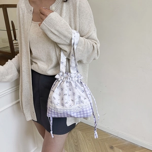 Floral and checkered drawstring bucket bag with lace trim and long handles shown on a model