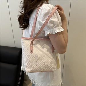 Elegant embroidered beige tote bag with pink trim and white tassel shown on shoulder