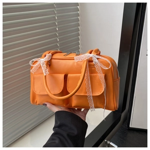 Détail d'un sac oreiller orange vif avec nœuds en dentelle blanche et poches avant à rabat