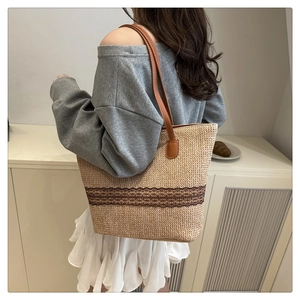 Detail of woven straw tote bag with brown leather handles and decorative ribbon trim