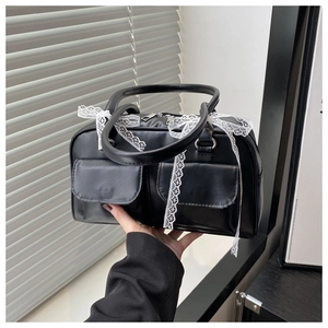 Détail du sac polochon en similicuir noir avec rubans en dentelle blanche et deux poches