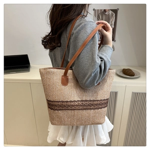 Close-up of woven straw tote bag with brown embroidery and faux leather handles