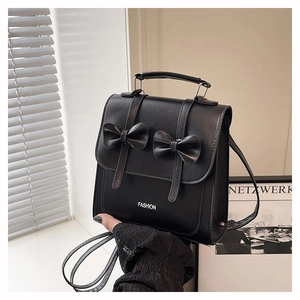 Detail showing the double bow decoration and fashion text on a black leather handbag
