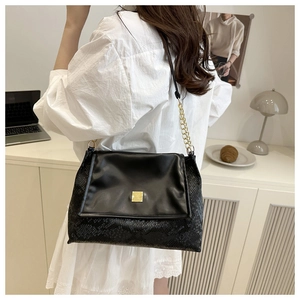 Detail shot of a black snakeskin pattern shoulder bag with a gold buckle on a model
