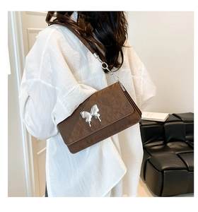 Close-up of brown textured shoulder bag with silver liquid metal butterfly and chain strap