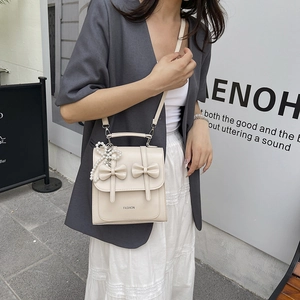 Creamy white crossbody bag with 3D bows and pearl charm on a minimalist urban background