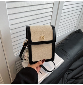 Detailed shot of beige woven phone bag with black flap and gold clover buckle