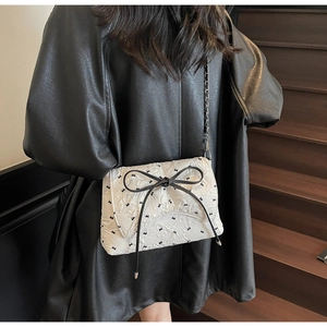 Close-up of white quilted crossbody bag with black bow tie and silver chain strap