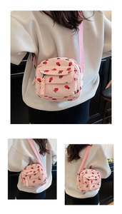 Detail of pink corduroy crossbody bag featuring red strawberry prints and a woven tassel