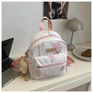 Close-up of white mini backpack with pink butterfly prints and plush bear charm detail