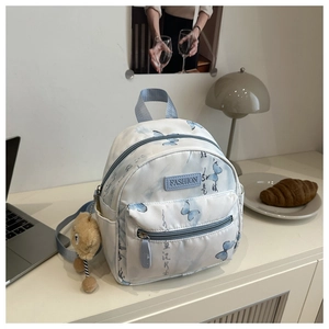 Close-up of white mini backpack featuring blue butterfly prints and a cute plush bear charm