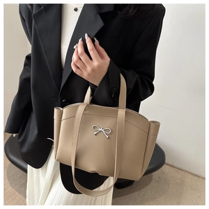 Detail of a khaki bucket bag featuring a silver metal bow buckle and smooth leather texture