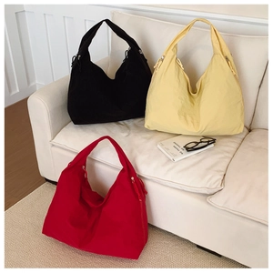 Trois sacs hobo en nylon minimalistes en noir, jaune et rouge sur un canapé blanc