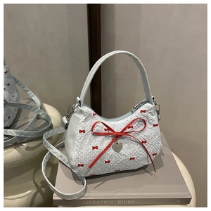 Close-up of heart charm and red ribbon bow on a contrast crescent handbag