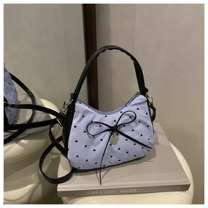 Detail of blue striped handbag featuring black heart polka dots and a bow pendant