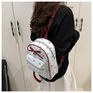 Detailed view of small white backpack with red bow patterns and heart charm on a model