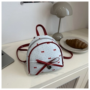 Detail of mini polka dot canvas backpack with red heart charm and bow accent on white desk