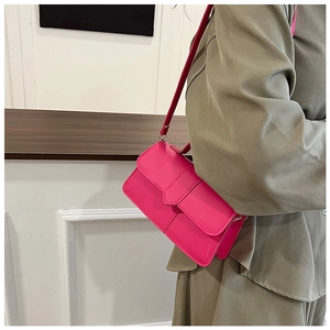 Detail view of a rose red crossbody bag with flap closure on a khaki outfit