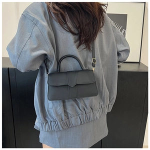 Modern black minimalist crossbody bag shown worn over a grey oversized blazer