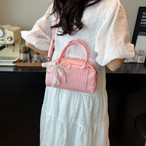 Pink Boston bag with pearl bow and lace detail shown on a model in a cafe setting