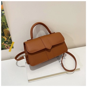 Chic caramel PU leather crossbody bag with geometric flap detail on an art book