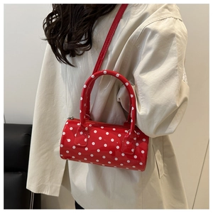 Detailed view of red polka dot cylinder bag worn cross-body on a model