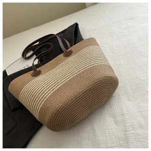 Close-up of striped raffia weave texture and brown faux leather handles on tote bag