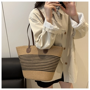 Detail view of woven straw bucket bag with black stripes and brown leather straps