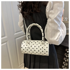 Close-up of white cylindrical polka dot handbag with black spots and sleek strap