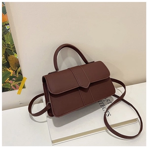 Close-up of a small dark brown square handbag with elegant V-shaped trim on white books