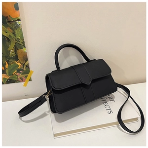 Detail view of black square handbag with top handle and adjustable strap on books