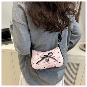 Detailed close-up of a pink underarm bag featuring black bow patterns and silver heart charm